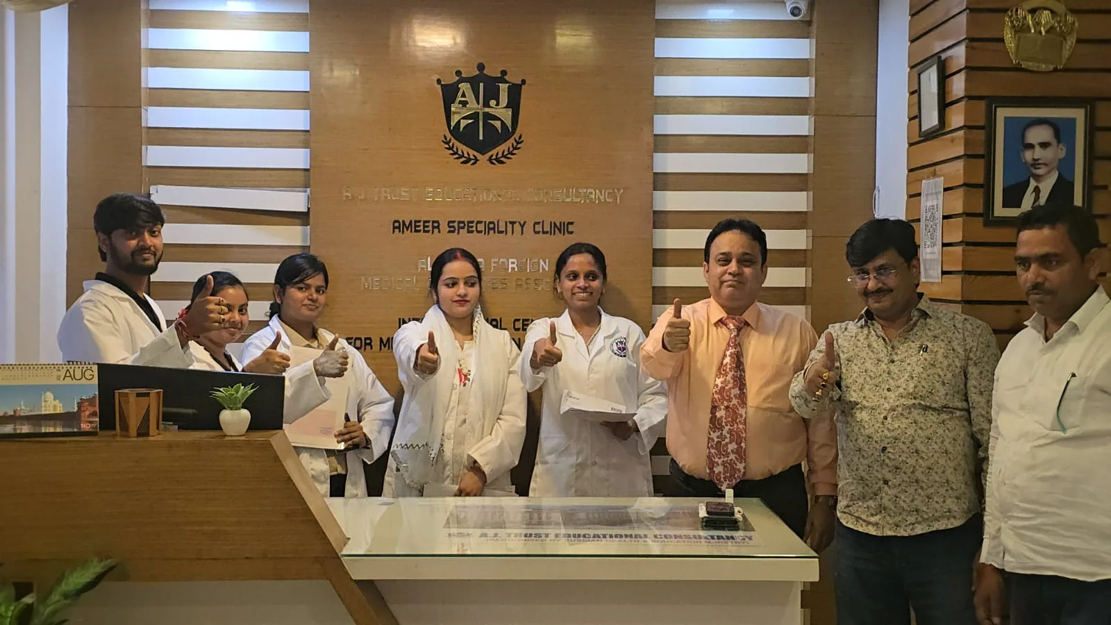 Students in white coats and A.J Trust staff giving a thumbs-up at the reception desk of an A.J Trust office